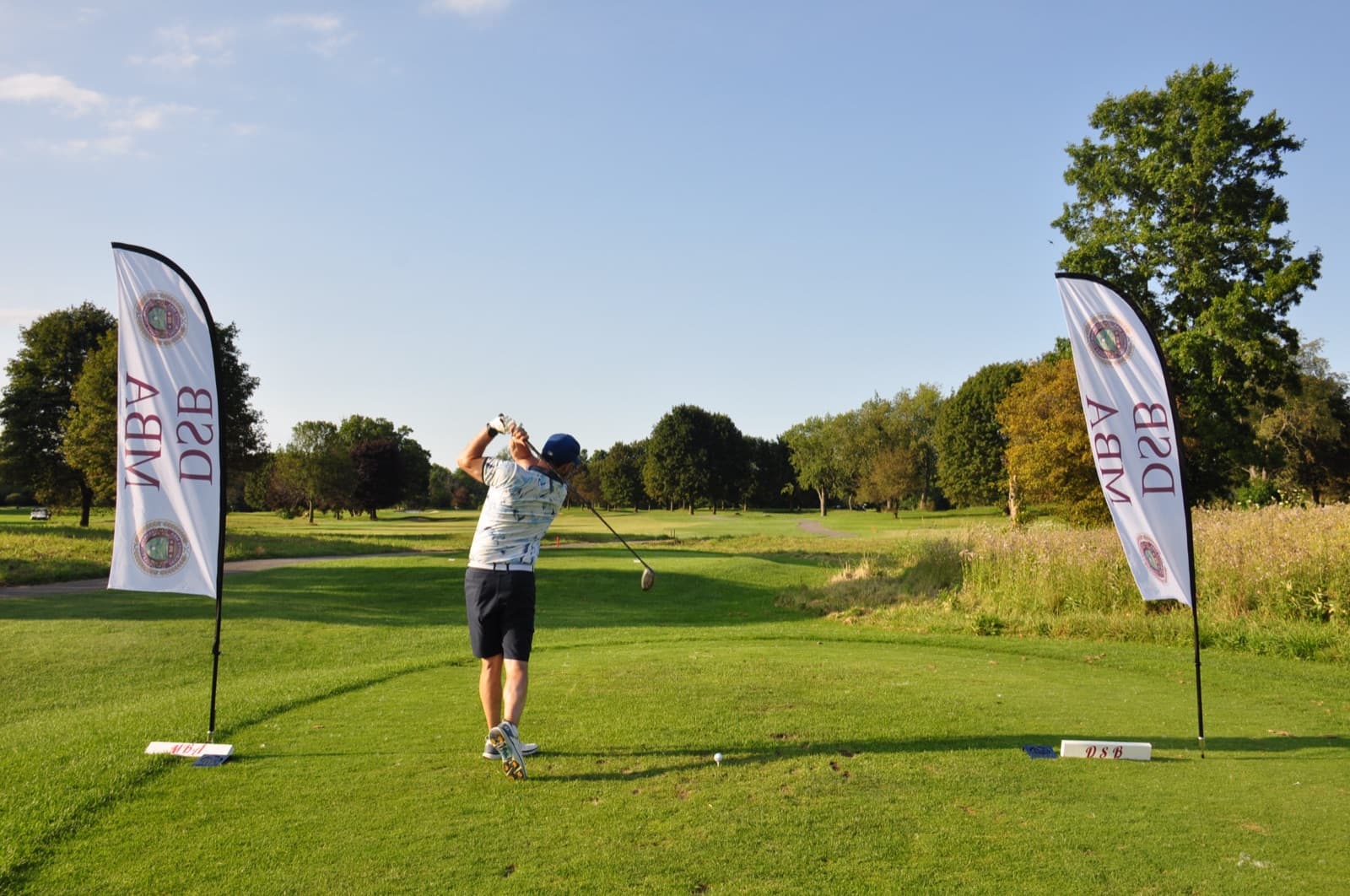 Golfer teeing off between two tall tournament feather flags